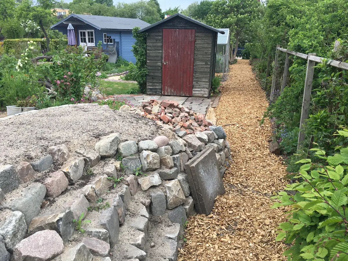 Steinstufen führen auf die Mauer und ein Pfad aus gehäckseltem Eichenholz zur Gartenpforte